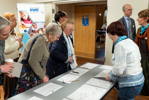 Mehrere Personen stehen an einem Tisch und füllen Formulare bei einer Veranstaltung aus.
