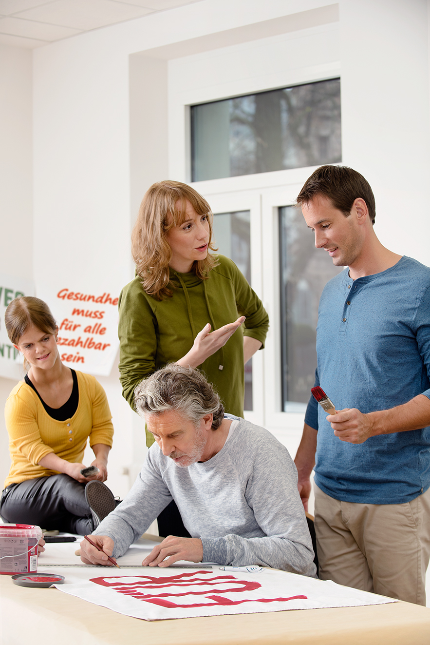 Zwei M&auml;nner und zwei Frauen malen gemeinsam Demo-Pappen f&uuml;r eine Demo, sie unterhalten sich. 