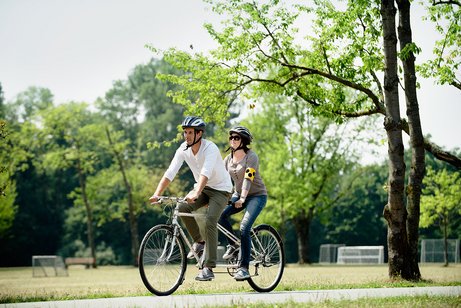Ein Mann und eine Frau fahren auf einem Tandem, sie hat eine Blinden-Armbinde um.