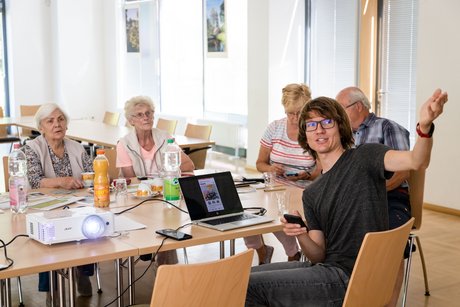 Eine Gruppe von 5 Personen sitzt an einem Tisch und tauscht Ideen in einer freundlichen Atmosphäre aus.