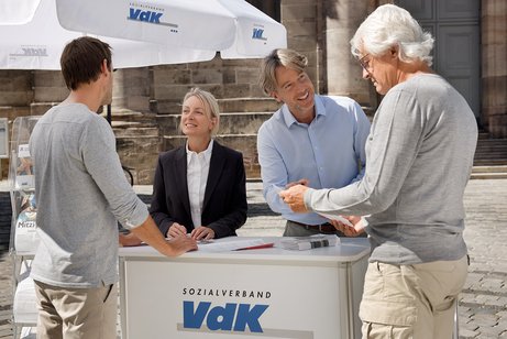 Eine Mitarbeiterin und ein Mitarbeiter an einem VdK-Infostand informieren gerade zwei interessierte Passanten. 
