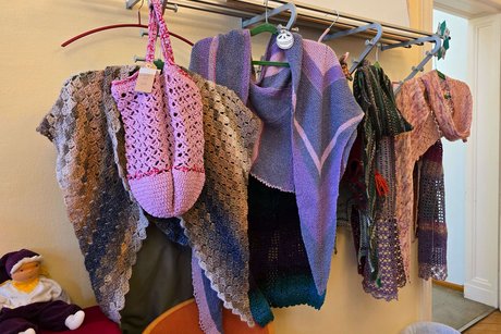 KV Steglitz-Zehlendorf Basar 2024 Handgestrickte und gehäkelte Kleidungsstücke und Accessoires in verschiedenen Farben hängen an einem Metallgestell in einem Raum mit Holzboden