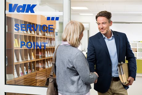 Ein VdK-Mitarbeiter begr&uuml;&szlig;t eine &auml;ltere Frau an der T&uuml;r einer VdK-Beratungsstelle. Er hat eine Aktenmappe unter dem Arm. 