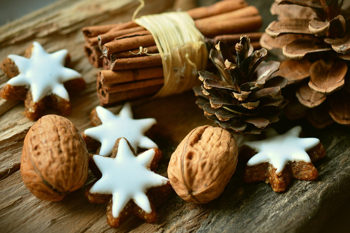 Eine Holzplatte belegt mit Walnüssen, Zimtstangen, Keksen und Kienäpfeln